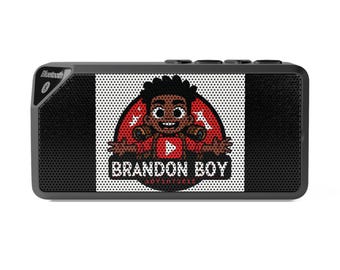 Puede incluir: Altavoz Bluetooth rectangular negro con un gráfico de un niño de dibujos animados en un círculo rojo con el texto "BRANDON BOY ADVENTURES". El altavoz tiene una parte frontal de malla negra y un símbolo Bluetooth.