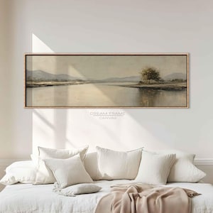 Könnte beinhalten: Ein rechteckiges Landschaftsgemälde mit einer ruhigen Flussszene, Bergen im Hintergrund und einem Baum auf der rechten Seite. Das Kunstwerk ist in einem dünnen, hellbraunen Rahmen gerahmt. Der Text "DREAM FRAME CANVAS" ist unten aufgedruckt.