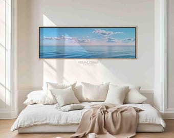 Puede incluir: Una impresión en lienzo rectangular enmarcada que representa una serena escena oceánica con cielo azul y nubes blancas. La impresión está montada sobre un sofá cama blanco con almohadas y una manta beige. El texto "DREAM FRAME CANVAS" es visible.