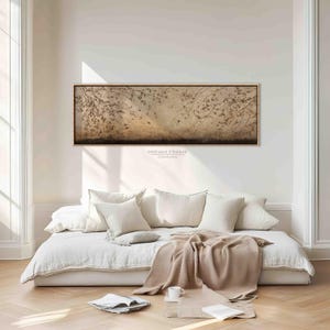 May include: A rectangular framed canvas art piece with a neutral color palette hangs above a white daybed. The artwork features a muted brown and beige abstract design with a dark brown border. The text "DREAM FRAME CANVAS" is visible.