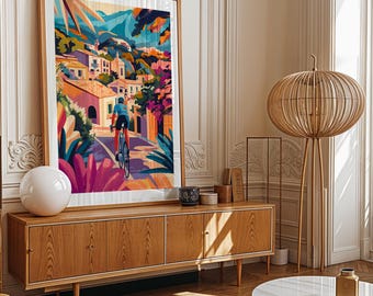 May include: A colorful illustration of a cyclist riding a bicycle up a hill in a town with buildings and trees. The illustration is framed and hanging on a wall above a wooden cabinet.