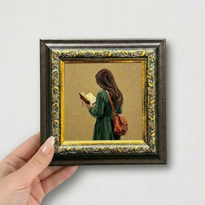 May include: A framed painting of a person reading a book, wearing a green dress and a brown satchel. The painting has a gold and dark brown ornate frame. The person is facing away from the viewer, with long brown hair.