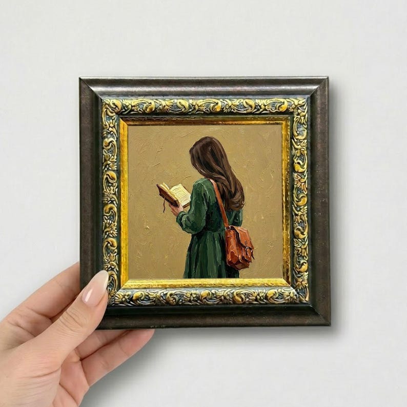 May include: A framed painting of a person reading a book, wearing a green dress and a brown satchel. The painting has a gold and dark brown ornate frame. The person is facing away from the viewer, with long brown hair.