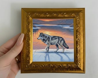 Puede incluir: Pintura al óleo enmarcada que representa un lobo gris caminando sobre la nieve, con una puesta de sol sobre un lago al fondo. El marco dorado ornamentado añade un toque de elegancia a la escena de la fauna.