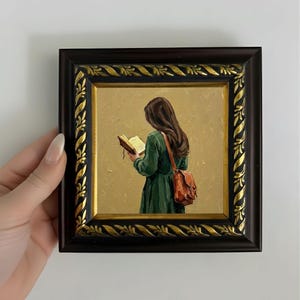 May include: A framed oil painting depicts a person reading a book. The person is wearing a green dress and carrying a brown satchel. The painting is in a dark brown frame with gold accents.