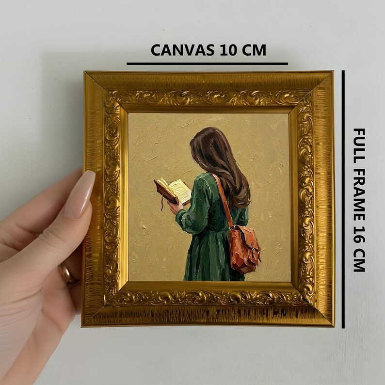 May include: A framed painting with a gold ornate frame. The painting depicts a person in a green dress reading a book, with a brown leather bag. The canvas is 10 cm, and the full frame is 16 cm.