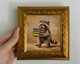 May include: A square painting in an ornate gold frame depicting a raccoon walking while carrying a stack of four books in red, blue, green, and yellow covers. The background is a soft, muted brown and tan wash with visible brushstrokes.