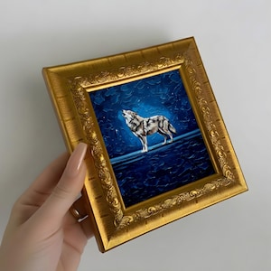 May include: A framed painting of a howling wolf under a starry night sky. The artwork features a gold ornate frame and a textured, dark blue background. The wolf is depicted in shades of gray and white.