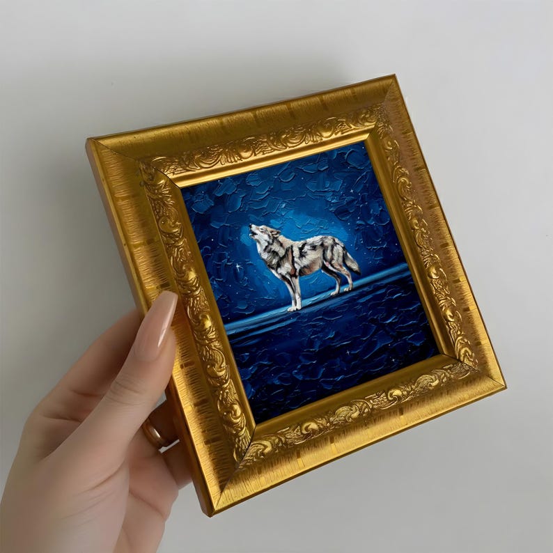 May include: A framed painting of a howling wolf under a starry night sky. The artwork features a gold ornate frame and a textured, dark blue background. The wolf is depicted in shades of gray and white.