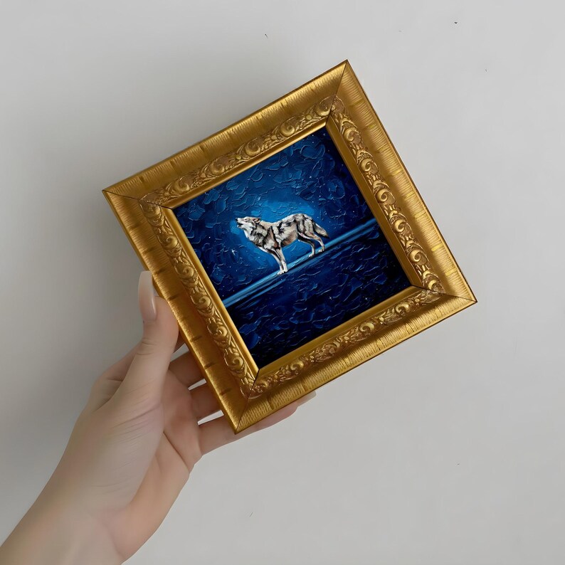 May include: A framed painting of a wolf howling at the moon. The artwork features a gold ornate frame and a dark blue background with a textured appearance. The wolf is depicted in shades of gray and white.