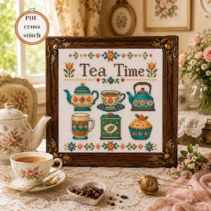 Può includere: Un motivo a punto croce incorniciato con il testo Tea Time, una teiera, una tazzina, un bollitore, una tazza, una scatola da tè e un cupcake. Il design utilizza fili arancioni, verde acqua e verdi su tessuto bianco, in una cornice di legno decorata.