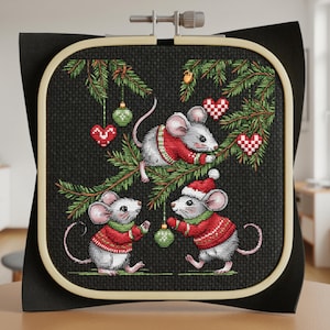 May include: Cross-stitch embroidery showing three mice in red sweaters and Santa hats, decorating a Christmas tree. The mice are grey with pink ears and tails. The tree has green needles and is decorated with green baubles and red heart-shaped decorations.