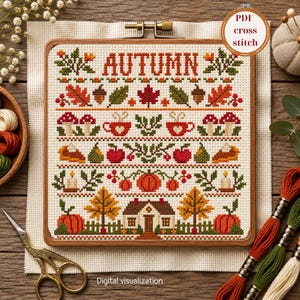 Könnte beinhalten: Ein quadratisches Kreuzstichmuster in einem Holzrahmen mit dem Wort AUTUMN in roten Buchstaben, umgeben von Motiven aus Blättern, Eicheln, Pilzen, Tassen, Äpfeln, Birnen, Kürbissen, Kerzen, Bäumen und einem Haus auf weißem Aida-Stoff.