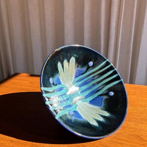 May include: A ceramic bowl with a dark blue exterior and a vibrant interior design. The interior features a white and turquoise floral pattern with blue accents. The bowl is placed on a wooden surface.