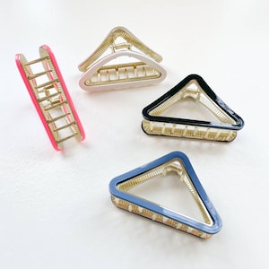 May include: Four hair clips in different colors and shapes. One is pink and rectangular, one is white and triangular, one is black and triangular, and one is blue and triangular.