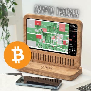 May include: A wooden crypto tracker with a screen displaying stock market data. The screen shows green and red blocks representing stock performance. The time and weather are displayed on the right. A Bitcoin logo is in the foreground. The text "CRYPTO TRACKER" is at the top.