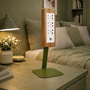 May include: A wooden power strip with four sockets and a USB port, mounted on a green metal stand. The power strip is rectangular with a light wood grain finish. The stand has a square base and a vertical support.