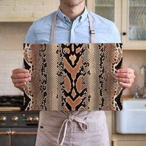 May include: A person holding up a kitchen towel with a brown and black snake skin pattern.