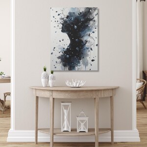 Op de afbeelding: Abstracte kunstprint met een silhouet van een persoonsprofiel met een donkerblauw en grijs aquareleffect. Het kunstwerk wordt tentoongesteld op een witte muur boven een houten console met decoratieve items.