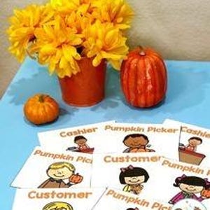 May include: An orange pumpkin and a smaller pumpkin sit on a blue surface next to a vase of yellow flowers. Several role-playing nametags with the text "Pumpkin Picker" and "Cashier" are displayed. The words "PUMPKIN PATCH" are at the top.