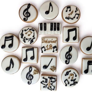 Pode incluir: Uma coleção de 18 biscoitos com tema musical decorados com glacê preto e dourado. Os biscoitos apresentam notas musicais, claves de sol e um teclado de piano.