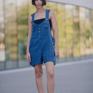 Könnte beinhalten: Eine Frau trägt einen blauen Denim-Overall mit Knöpfen und schwarzen Sandalen.