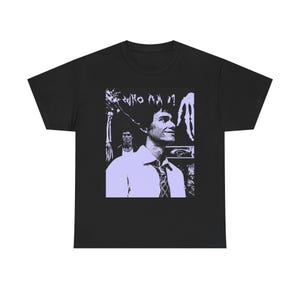 Può includere: T-shirt nero con una stampa grafica viola di un uomo con il testo "WHO AM I!" stampato sulla maglietta.