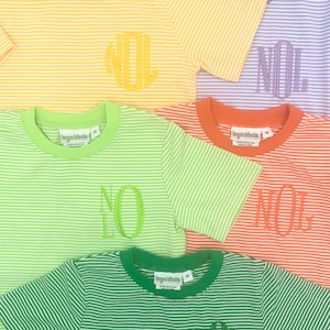 May include: A collection of striped t-shirts in various colors, including yellow, orange, green, and purple. Each shirt features an embroidered monogram. The shirts have short sleeves and a crew neck.