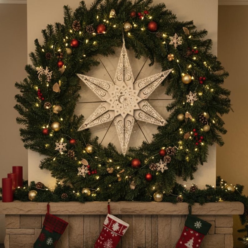 May include: A large Christmas wreath with a white star in the center, decorated with red and gold ornaments, pinecones, and lights. Below, a stone mantel displays three Christmas stockings.