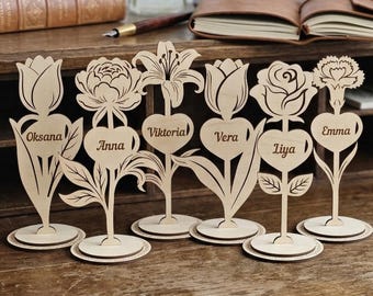 May include: A white ceramic mug with a black handle and the text "But First, Coffee" in a bold, black font. The mug is set against a blurred background, suggesting a cosy setting.