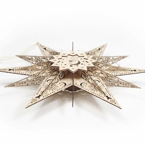 May include: A wooden star-shaped decoration with intricate cut-out designs of moons, stars, and celestial patterns. The natural wood color is accented by small lights strung around the star's points. The star is approximately 18 inches in diameter.
