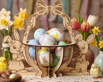 May include: A wooden Easter basket filled with decorated eggs, flanked by wooden bunny figures and daffodils. The basket has a bow-shaped handle. A small nest with eggs and a yellow chick are in the foreground.