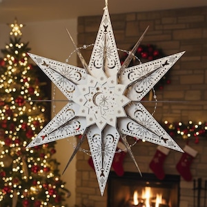May include: A large, cream-colored star-shaped Christmas ornament with intricate cut-out designs. The star features celestial motifs, including moons and stars, and is suspended in front of a Christmas tree and fireplace. The ornament is illuminated with small lights.
