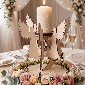 May include: A wooden angel candle holder with a lit, patterned candle. The candle holder features two angel figures and is surrounded by a floral arrangement of roses. The setting is a table, possibly for a wedding or special event.