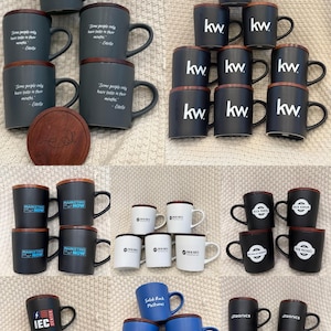 May include: A collection of ceramic mugs with wooden lids. The mugs are in various colors, including dark gray, black, white, and blue. Some mugs have text such as "kw", "Marketing Now", "IEC", and "Solid Rock Pastures".