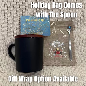 May include: A black mug with a wooden lid, a stainless steel spoon, and a burlap bag with a "Merry Christmas" design. A "Thank You" card is also included. Text on the image reads "Holiday Bag Comes With The Spoon" and "Gift Wrap Option Available."