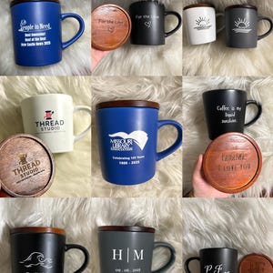 May include: Collection of ceramic mugs with wooden lids. Mugs are various colors, including blue, black, white, and gray. Some mugs have text like "People in Need" and "Coffee is my liquid sunshine." Others feature initials or logos. The lids are engraved.