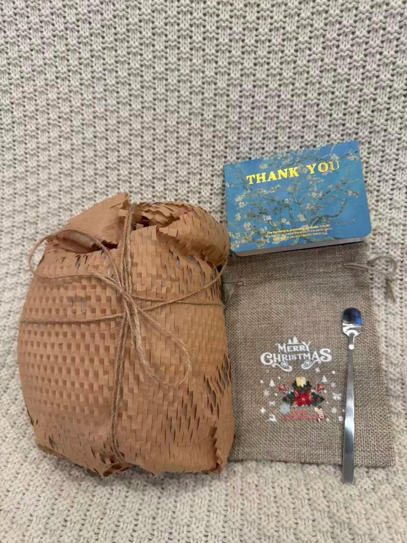 May include: A gift set with a wrapped package, a small burlap bag with "Merry Christmas" text and a spoon, and a blue "Thank You" card with a floral design. The wrapped package is tied with twine.