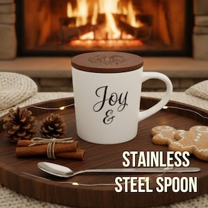 May include: White mug with a brown lid, featuring the word "Joy &" in black script. The mug sits on a wooden tray with a stainless steel spoon, cinnamon sticks, pine cones, and a gingerbread cookie. The text "STAINLESS STEEL SPOON" is below.