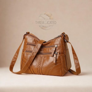 May include: A brown leather crossbody bag with multiple zippered compartments and a braided accent. The bag has an adjustable shoulder strap and the text "THREADICATED" in a circular design.