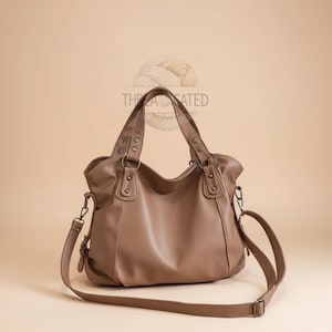 May include: A brown leather handbag with two top handles and a detachable shoulder strap. The bag has a rounded shape with metal hardware accents and the word "THREADATED" is printed on the top.