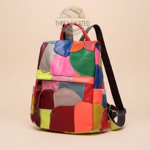 May include: A multi-colored leather backpack featuring a patchwork design of various shapes in shades of red, pink, green, blue, orange, yellow, and grey. The bag includes a top handle, two dark brown shoulder straps, and a front zipper closure.