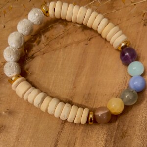 Könnte beinhalten: Ein Armband aus weißen Lavasteinen und Holzperlen mit einem Regenbogen aus Edelsteinen, darunter Amethyst, Aquamarin, blauer Spitzenachat, grüner Aventurin, Citrin und Rosenquarz.