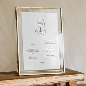 K&ouml;nnte beinhalten: Eine goldene Speisekarte mit einem Cocktailbar-Logo und einer Getr&auml;nkekarte in deutscher Sprache. Die Speisekarte steht auf einem Holzst&auml;nder.