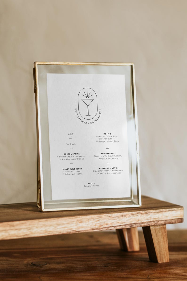 K&ouml;nnte beinhalten: Eine goldene Speisekarte mit einem Cocktailbar-Logo und einer Getr&auml;nkekarte in deutscher Sprache. Die Speisekarte steht auf einem Holzst&auml;nder.