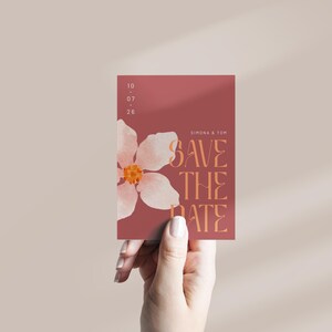 May include: A save the date card with a pink flower illustration and the text "Save the Date" in orange. The date is listed as 10.07.25. The names "Simona & Tom" are printed at the top of the card.