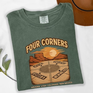 May include: Green Comfort Colors t-shirt with a graphic of the Four Corners monument. The graphic features a compass design with the states Arizona, Utah, Colorado, and New Mexico. The shirt has a crew neck.