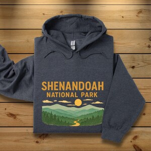 A dark charcoal gray hoodie is folded neatly on a wooden plank background, featuring a Shenandoah National Park graphic.