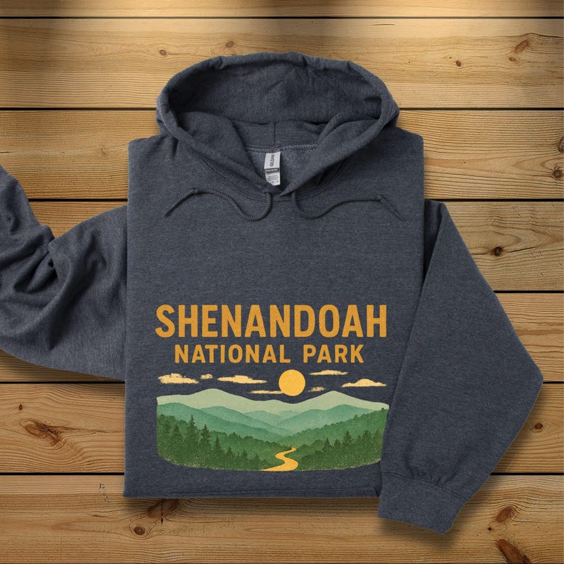 A dark charcoal gray hoodie is folded neatly on a wooden plank background, featuring a Shenandoah National Park graphic.