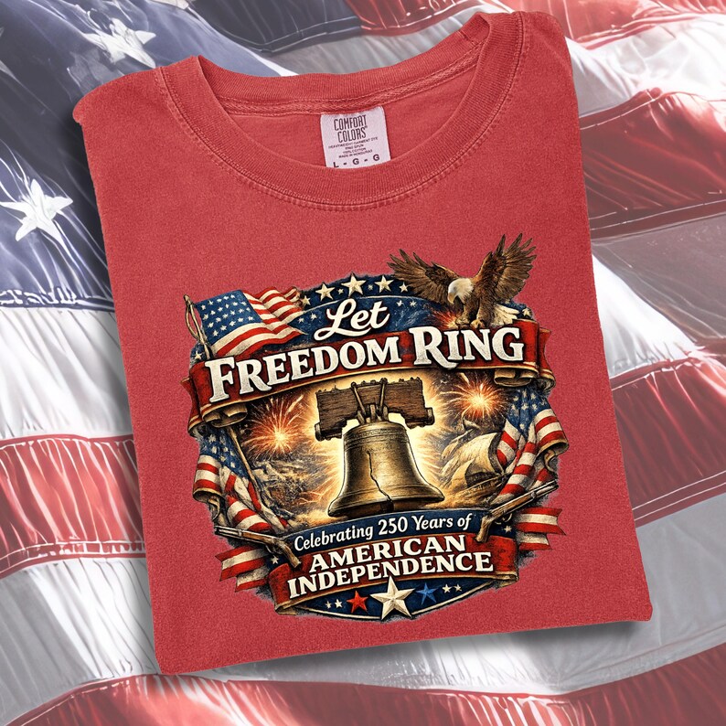 May include: A red t-shirt featuring a graphic print of the Liberty Bell, a bald eagle, and American flags. The text reads Let Freedom Ring and Celebrating 250 Years of American Independence. The shirt has a Comfort Colors brand label at the neck.
